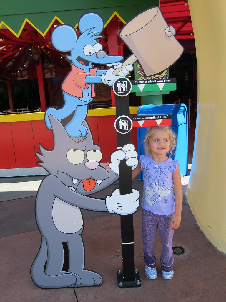 a girl standing against a sign with a line that says at least this tall to ride